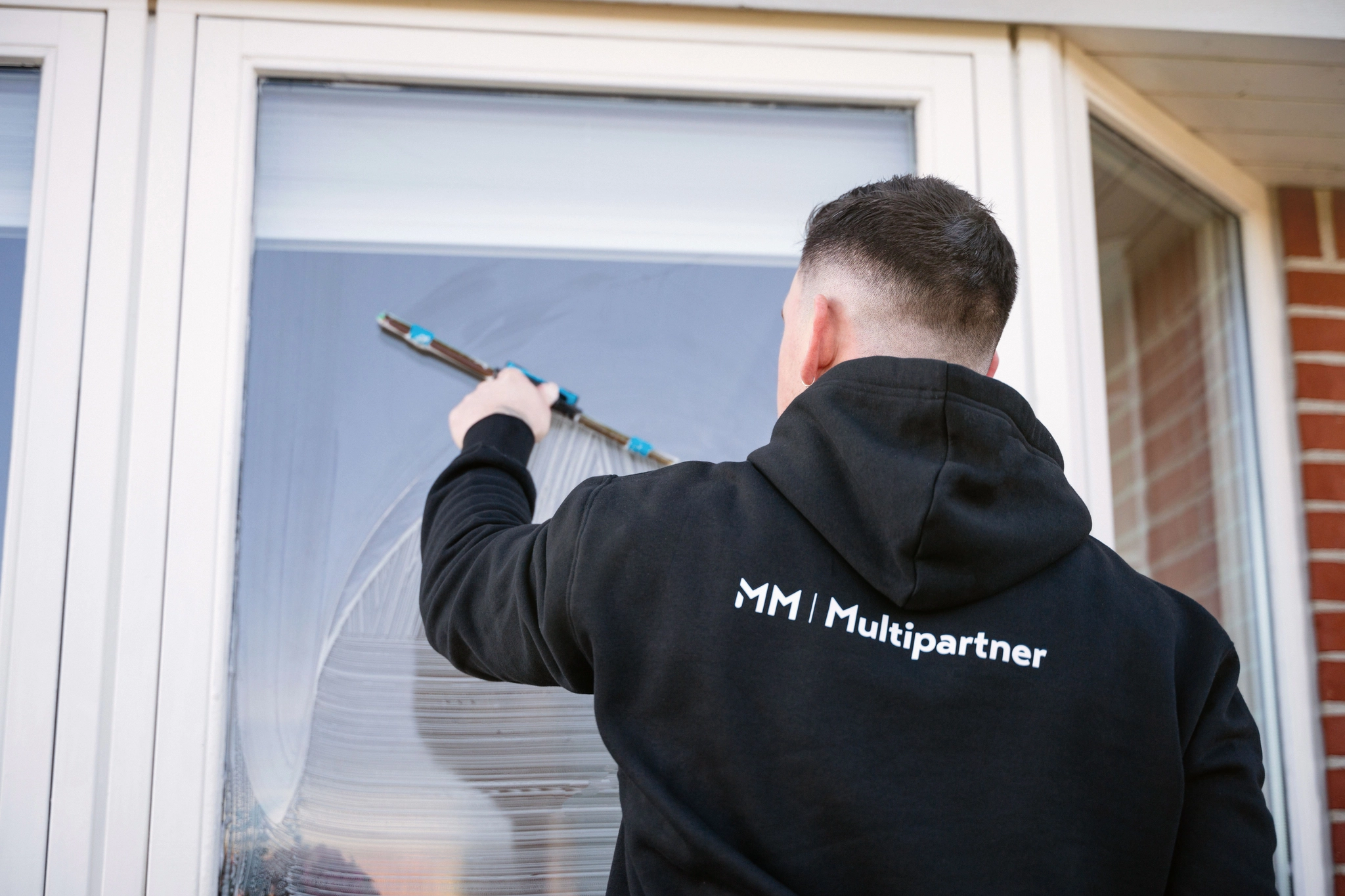 Mathias fra MM Multipartner pudser vinduer med skraber på 1. sal